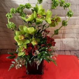 Tall floral arrangement with green orchids and red accents in a dark vase