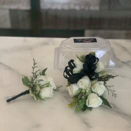 White rose boutonniere with black ribbon and greenery beside a clear plastic case