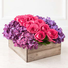 Pink roses arranged in a rustic wooden box with purple hydrangeas