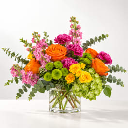 Bright mixed bouquet in a clear glass vase with orange, pink, yellow, and green blooms