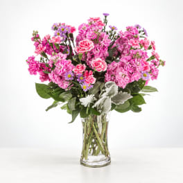 Pink mixed bouquet in a clear glass vase with purple accent flowers
