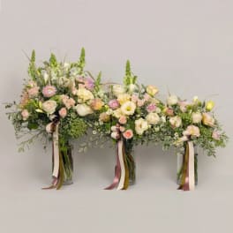 Three pastel floral arrangements in glass vases with ribbon streamers