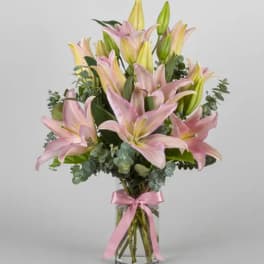 Pink and yellow lilies arranged in a clear glass vase with a pink ribbon