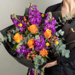 Bouquet of orange roses and purple flowers wrapped in black paper