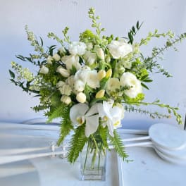 White floral arrangement in a clear glass vase with orchids and roses