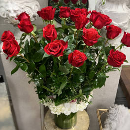 Red roses arranged in a clear vase with white flowers at the base