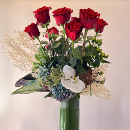 Red roses and a white orchid in a tall glass vase