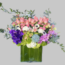Mixed bouquet of pink roses, orchids, and white blooms in a glass vase