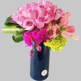 Pink roses, tulips, orchids, and hydrangea in a tall dark vase