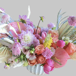 Pink and peach floral arrangement in a white vase with tropical leaves