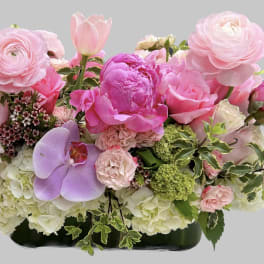 Pink floral arrangement with peonies, roses, tulips, and orchids in a low container