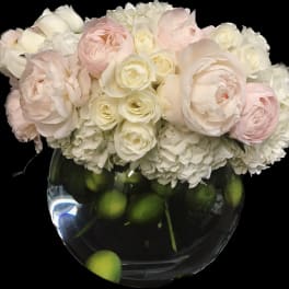 Blush and white flower arrangement in a round glass vase with green fruit inside
