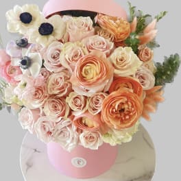 Bouquet of peach and pink roses with white anemones in a pink hatbox