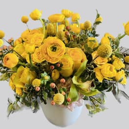 Yellow floral arrangement in a white vase with round blooms and berries