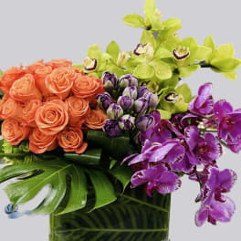 Bouquet of orange roses with green and purple orchids in a glass vase