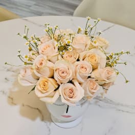 Peach rose bouquet in a white face-shaped vase with tiny daisy accents