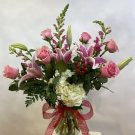 Pink roses and lilies arranged in a glass vase with a red striped ribbon.