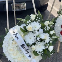 White funeral wreath with roses and a satin ribbon on an easel
