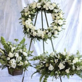 White wreath, spray, and matching floral arrangement on stands with green accents for a sympathy display.