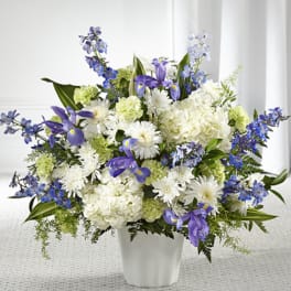 Tall arrangement of white hydrangeas, mums, green carnations and blue irises in a white vase