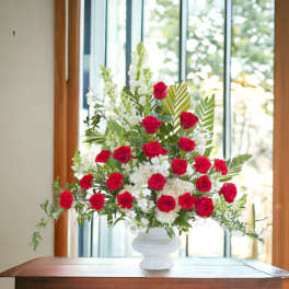 Tall arrangement of red roses and carnations with white flowers in a white urn on a table
