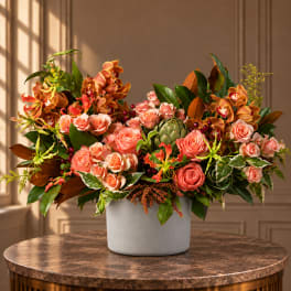 Large floral arrangement of peach roses and orange orchids in a white vase