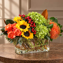 Mixed bouquet in a glass vase with sunflowers, roses, and green hydrangea