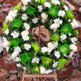 Circular floral wreath with white and green flowers on a wooden stand