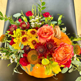 Fall floral arrangement in an orange pumpkin container with roses and mums