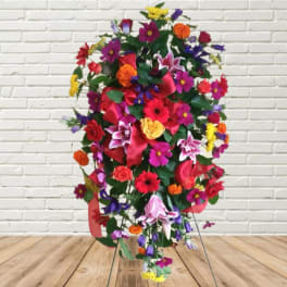 Tall colorful floral standing spray with mixed blooms and a red ribbon
