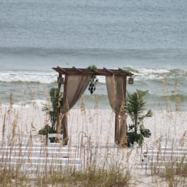 Beach wedding arch with draped curtains and chairs on the sand