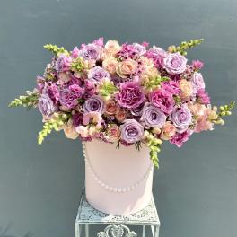 Lavender and pink rose arrangement in a pink hat box with pearls on a decorative metal stand.