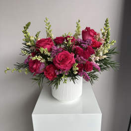 Bright pink rose and carnation arrangement with white snapdragons in a white ribbed ceramic vase.