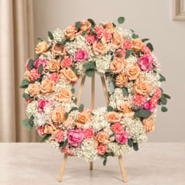Floral wreath on a wooden easel with peach, pink, and white blooms