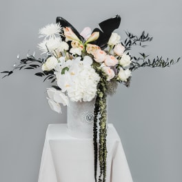 White and blush floral arrangement in a white hatbox on a draped pedestal