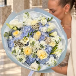 Woman holding a bouquet of blue and white flowers with pale yellow roses