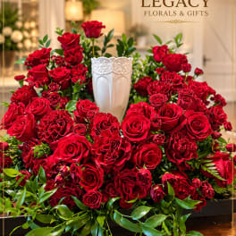 Large red rose arrangement in a white vase with trailing greenery
