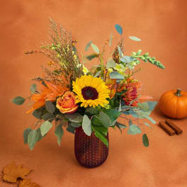 Autumn bouquet with a sunflower and orange blooms in a burgundy vase.