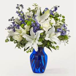 White lilies and blue flowers arranged in a cobalt vase