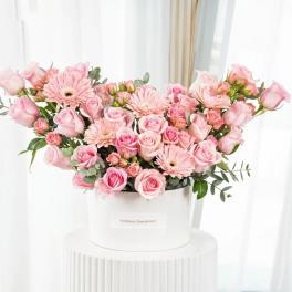Pink roses and gerbera daisies arranged in a white hatbox