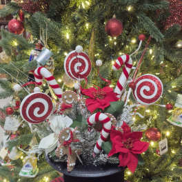 Christmas arrangement with candy canes, gingerbread figures, and red poinsettias in a black hat box