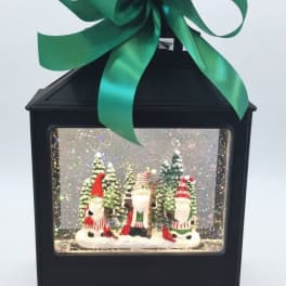 Black lantern with a large green bow and a Christmas gnome scene inside