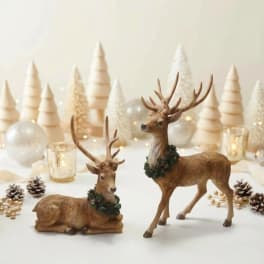 Two deer figurines with holiday decor and candles on a white surface