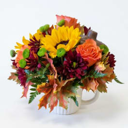 Bouquet of sunflowers, roses, and dark mums in a white mug