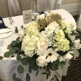 White floral centerpiece with roses and hydrangeas on a table
