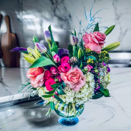 Pink and purple flower arrangement in a blue glass vase