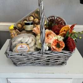 Gift basket with flowers, cookies, chocolates, and a candle in a wicker basket