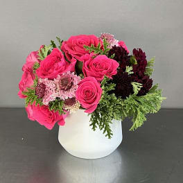 Pink roses and dark blooms arranged in a white vase
