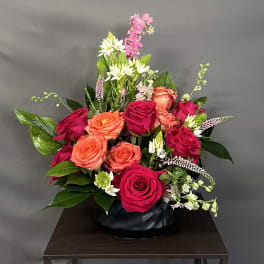 Mixed rose arrangement in a black vase with pink and orange blooms
