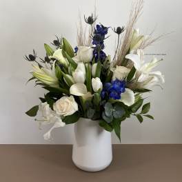 White lilies, roses, and blue flowers in a white vase